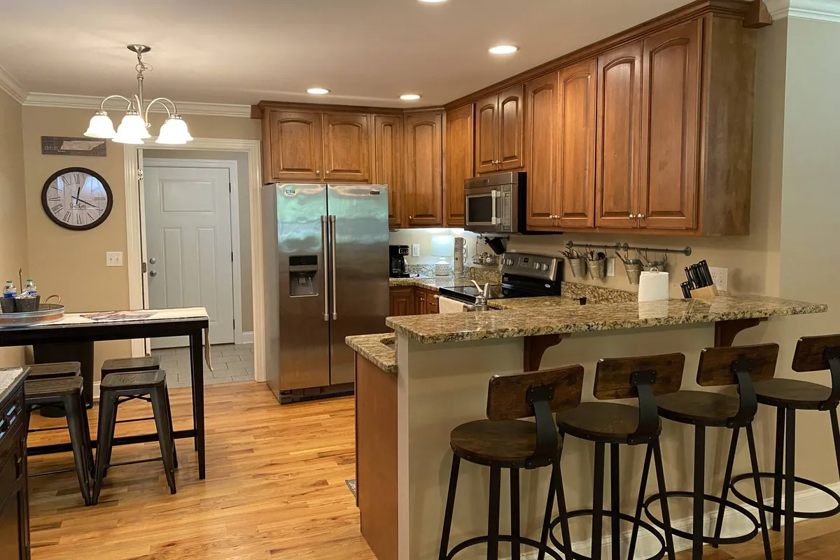 This image captures a warm, inviting kitchen with granite countertops, wooden cabinets, stainless steel appliances, and bar seating. The space is arranged to highlight its functionality and appeal for both cooking and socializing, with ample counter space and modern finishes.