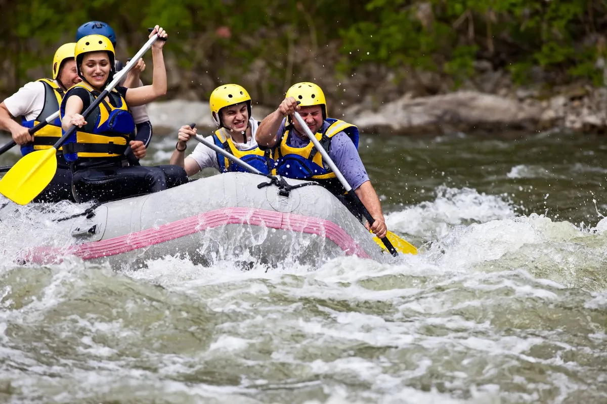 Groups of people navigate rushing river rapids in a rafting boat, paddles in hand, surrounded by the energy and excitement of outdoor adventure. The scene is lively, emphasizing shared experiences and team-building activities.