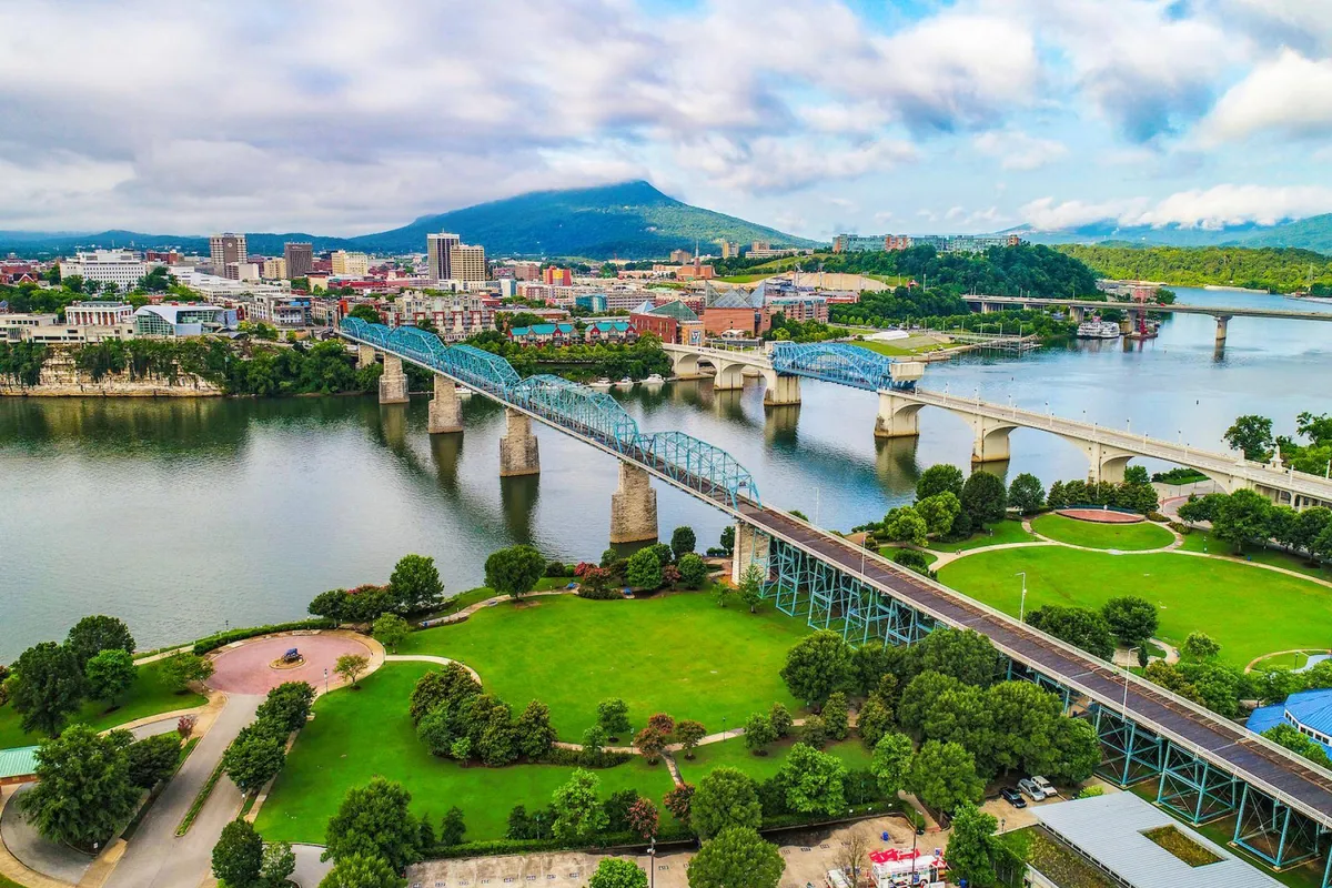 A sweeping vista captures the Tennessee River winding through the city, framed by iconic bridges, the urban skyline, and distant mountains under a serene sky.
