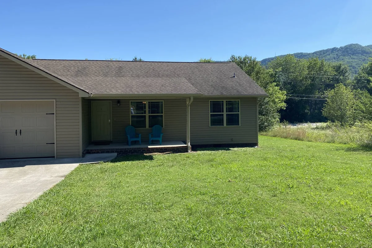 A wide view of the front porch with blue chairs, opening out onto a broad lawn and framed by a mountain backdrop. The scene suggests relaxation, enjoying nature, and the peace of the neighborhood after a busy event.