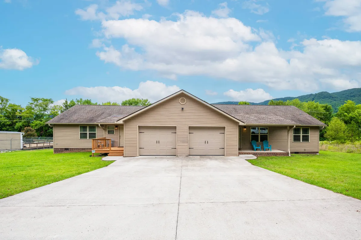 The home's inviting front porch features comfortable chairs, a view of the well-kept lawn, and surrounding trees. Garage doors and an accessible entry set a welcoming scene for group arrivals and easy access after festivities.
