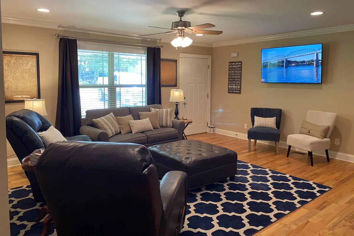 A cozy living room featuring a comfortable sofa, coffee table, area rug, television, and armchairs. The arrangement is open and inviting, ideal for socializing, movie nights, or gathering for games.